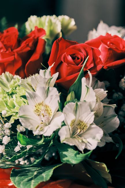 A floral arrangement featuring vibrant red roses with partially opened petals, paired with white alstroemeria lilies that have yellow and burgundy markings on their petals. The bouquet is wrapped in g